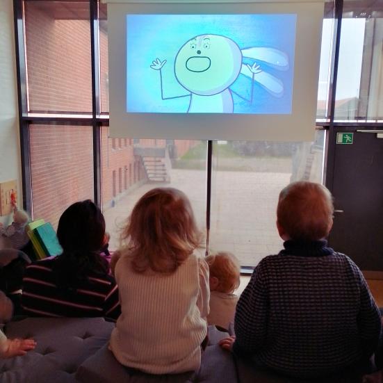 små børn med ryggen til ser film på stort lærred